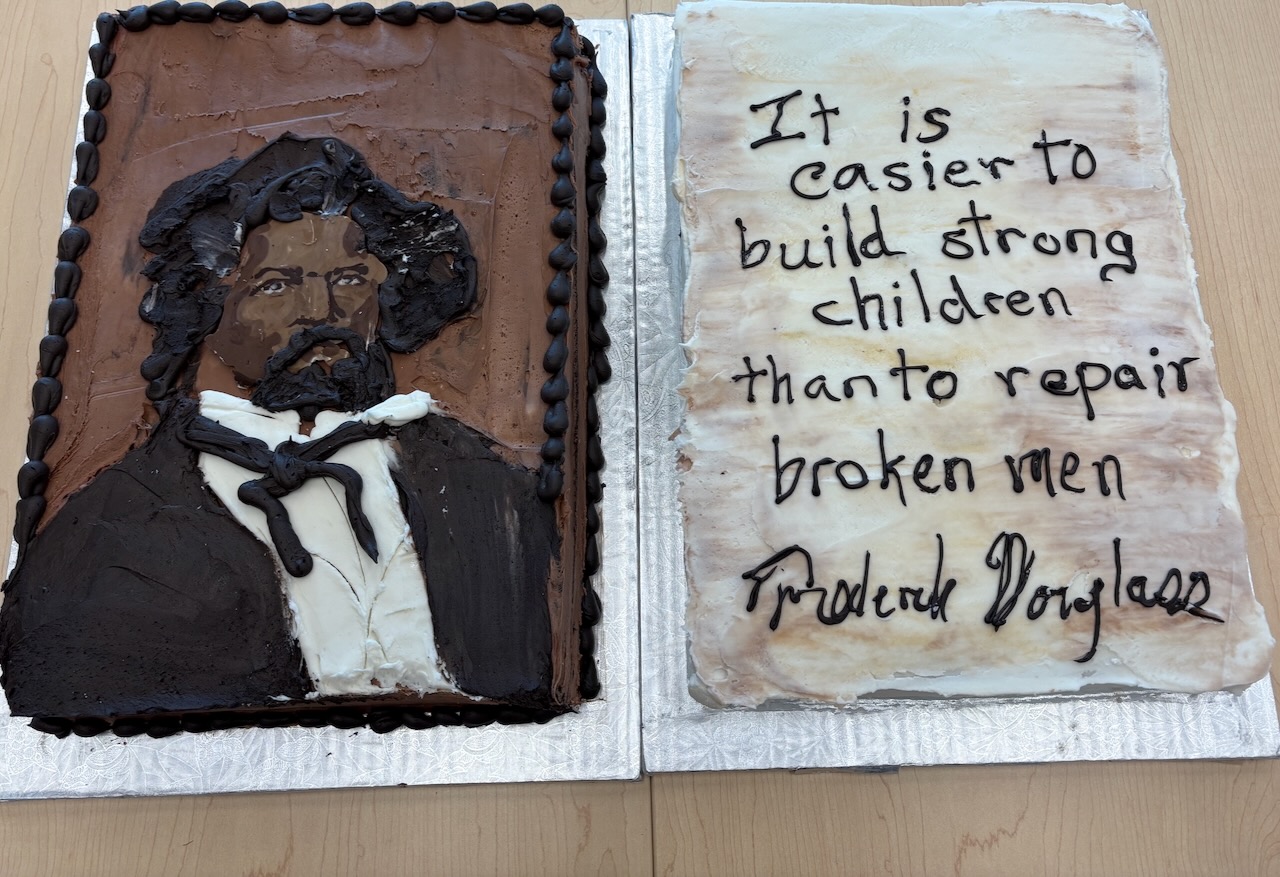 Two cakes, one decorated with the face of Frederick Douglass, the other with the words 'It is easier to build strong children than to repair broken men,' a quotation from Douglass