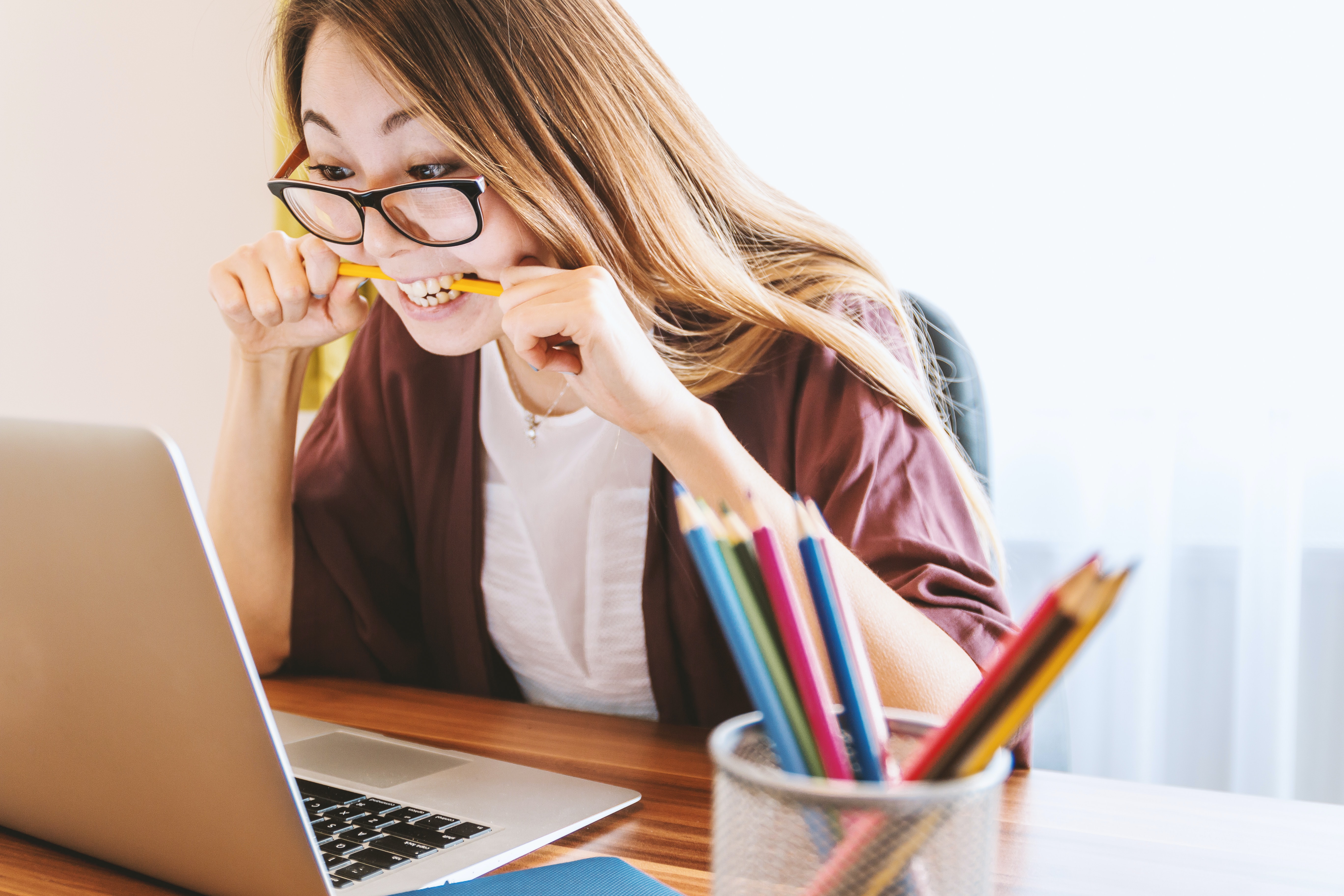 Woman biting pencil stressfully while looking at laptop screen